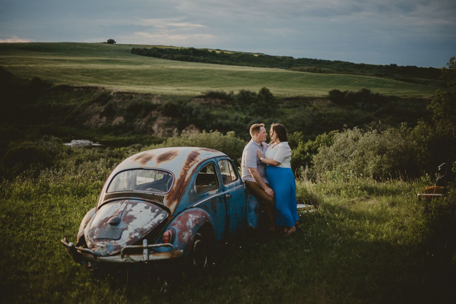 A vintage blue Volkswagen Beetle parked on a hilltop during a countryside photoshoot.