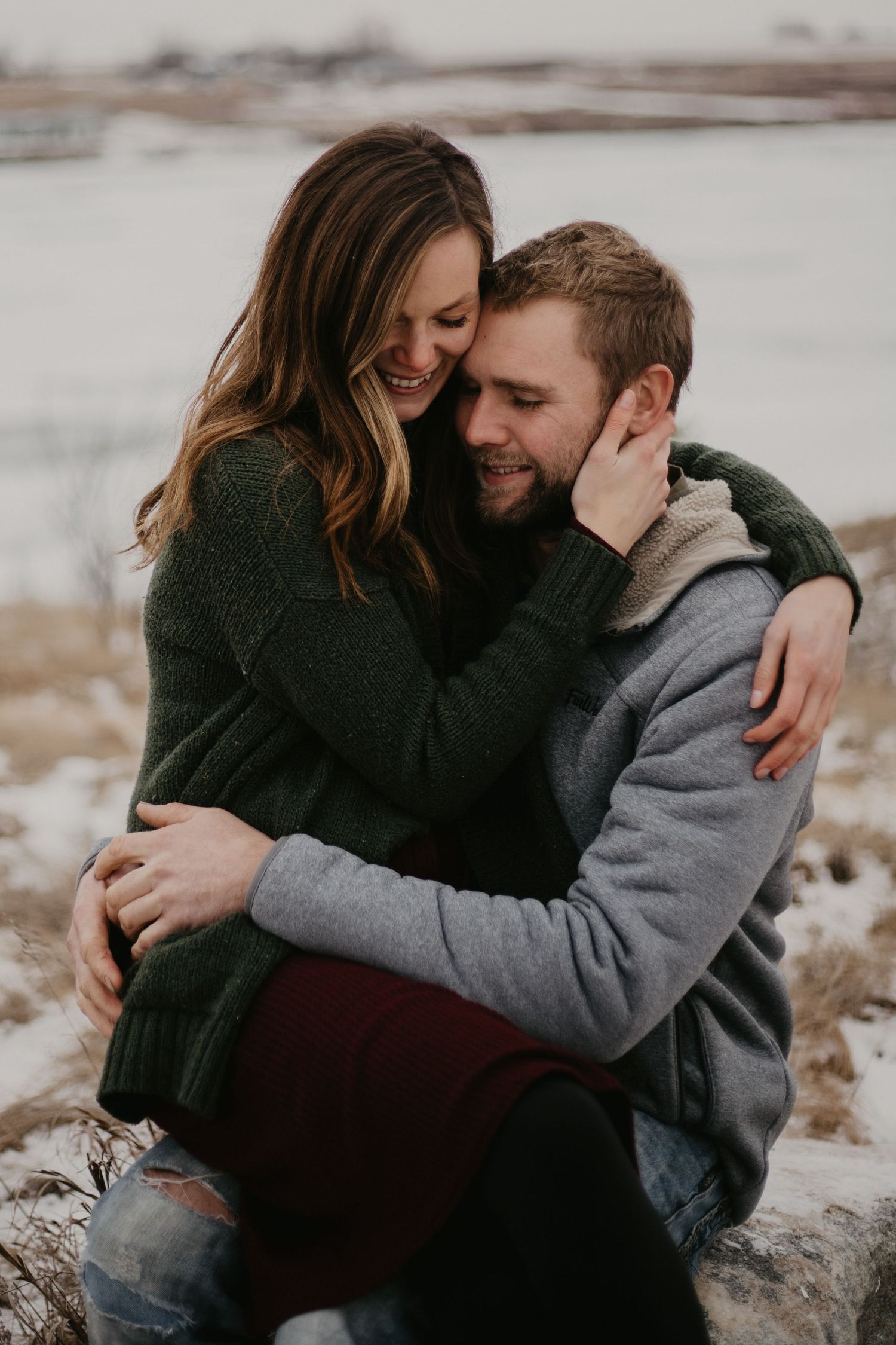 A couple shares an intimate embrace while sitting outdoors in winter clothing.