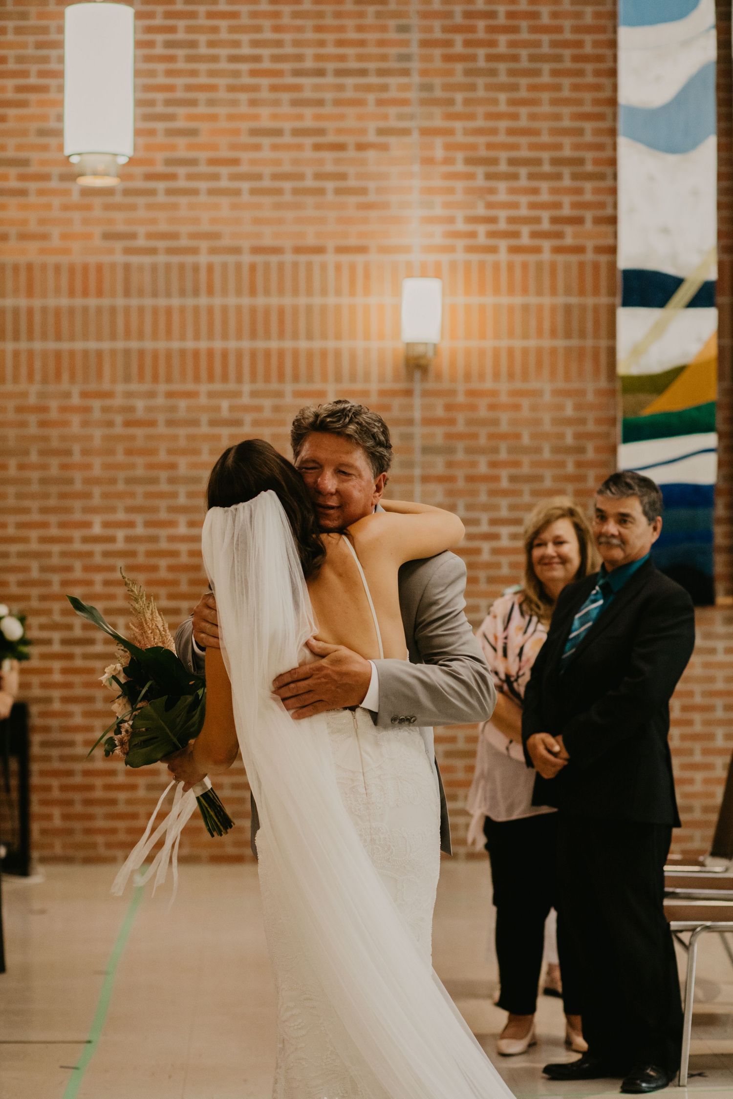 A couple shares a joyful embrace during their wedding ceremony in front of a brick wall and decorative mural.