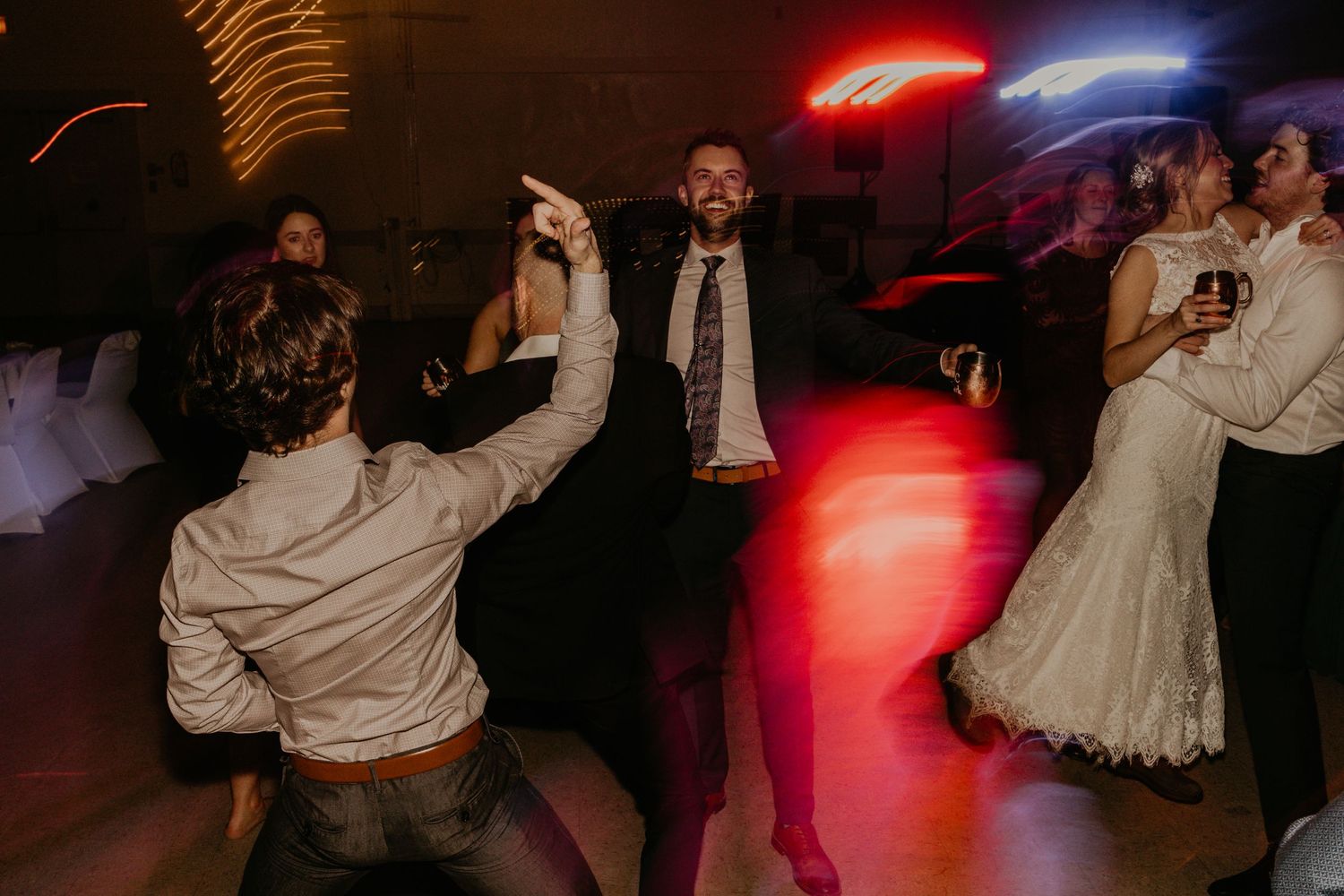 Wedding reception dance floor filled with celebrating guests under red and blue lighting.