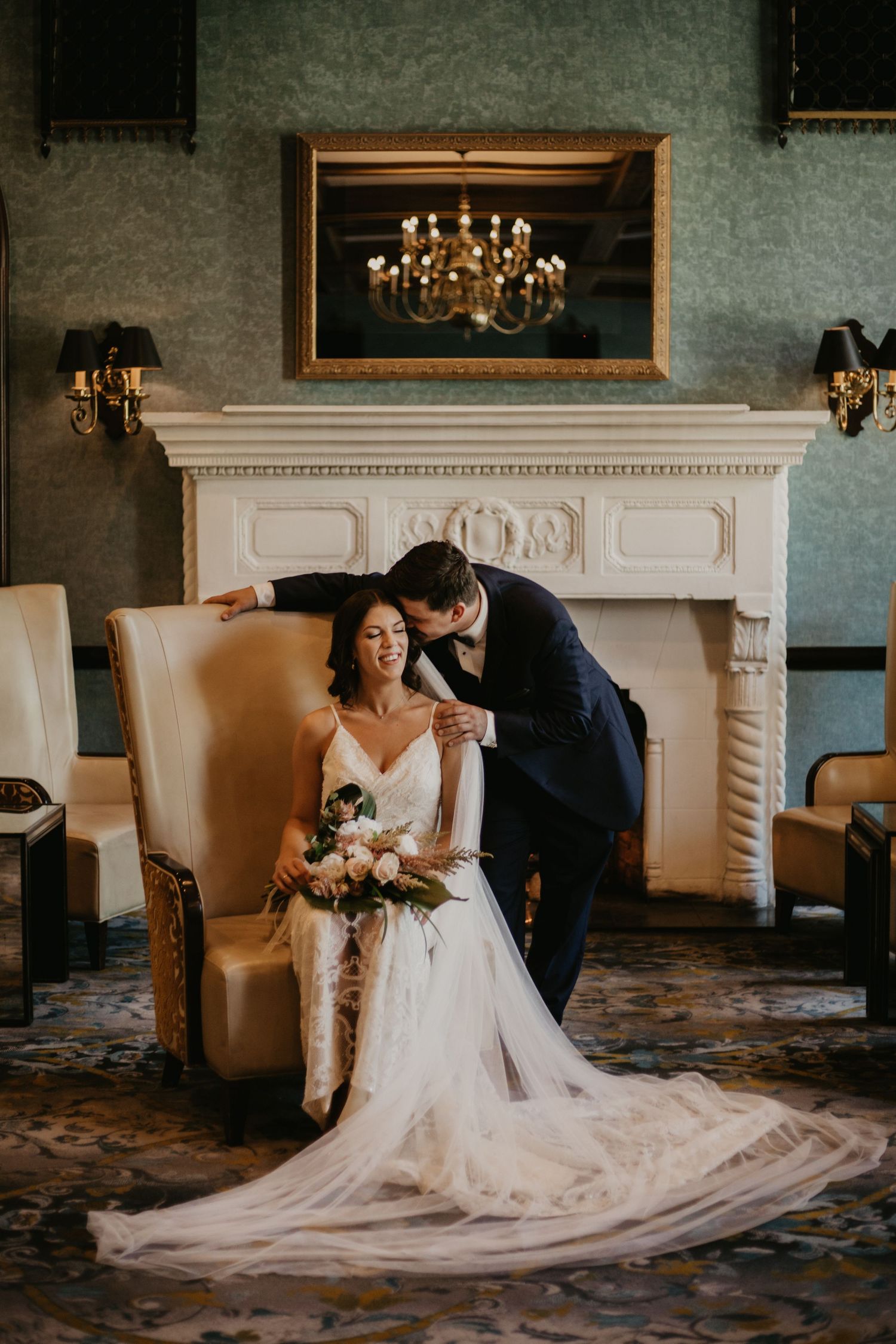 An intimate wedding portrait in a vintage room with an ornate fireplace and chandelier reflection.