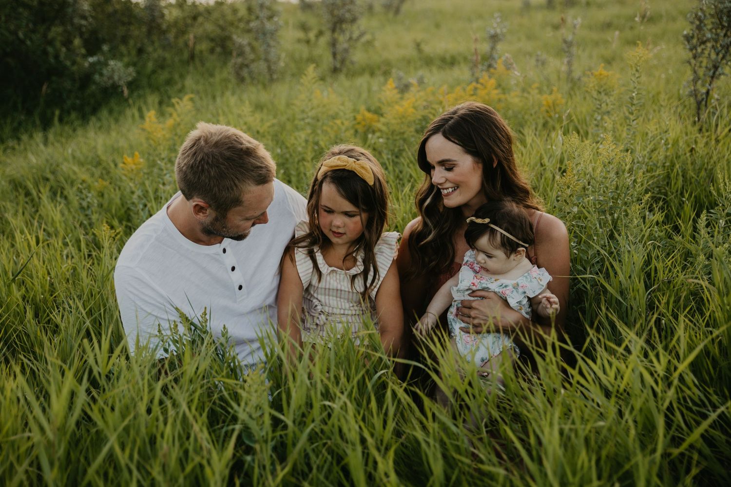 Family sitting together in tall grass field during sunset photo session.