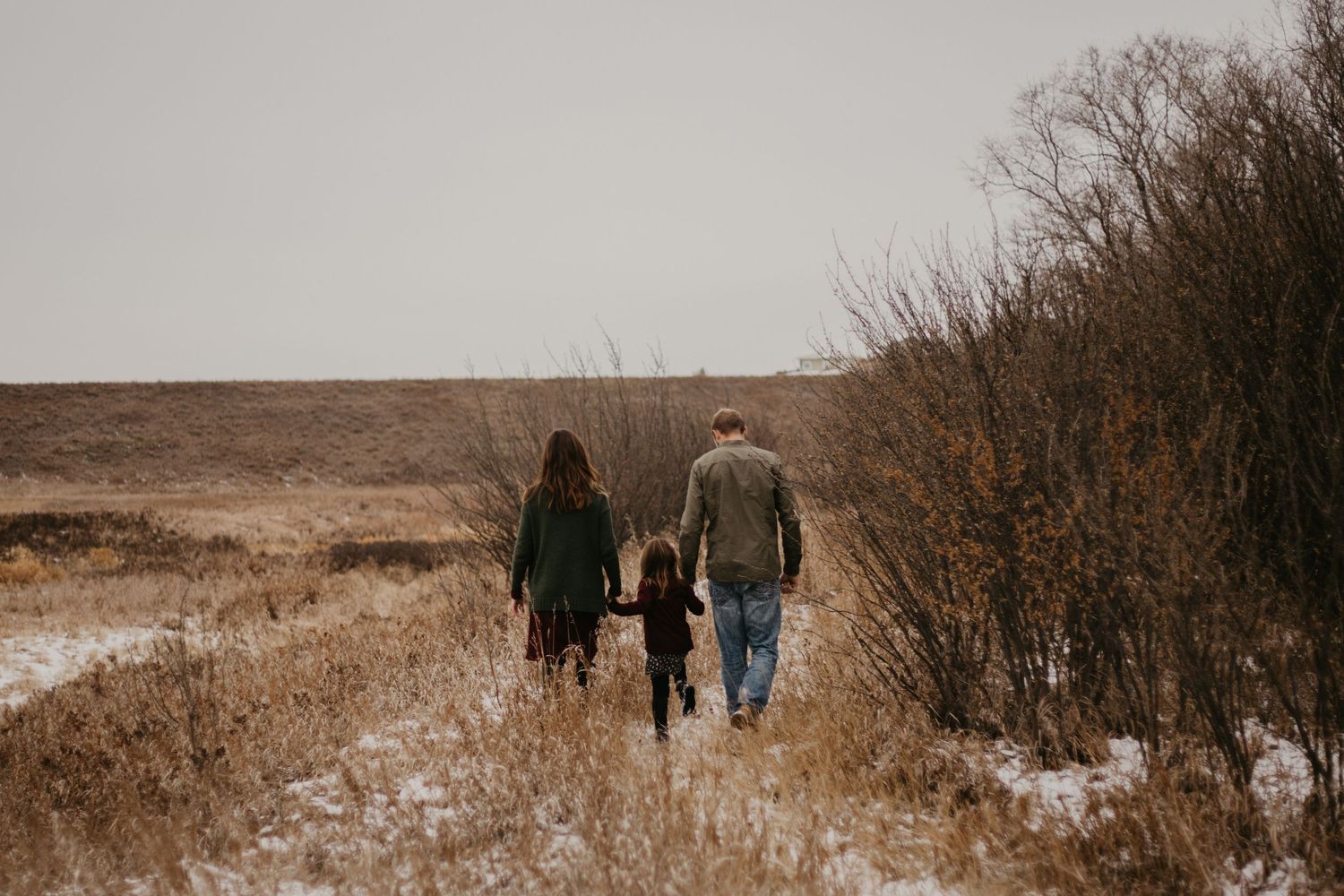 Family walking away from camera through a snowy winter field.