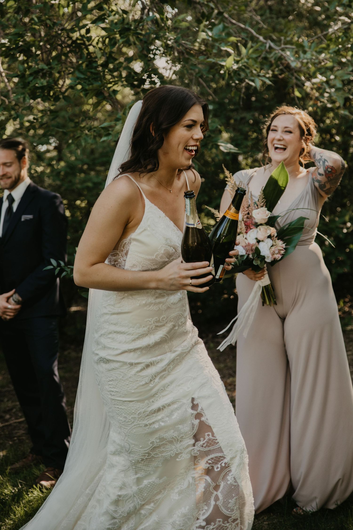 Joyful wedding celebration moment with bride and bridesmaid sharing laughs while holding drinks and bouquets.