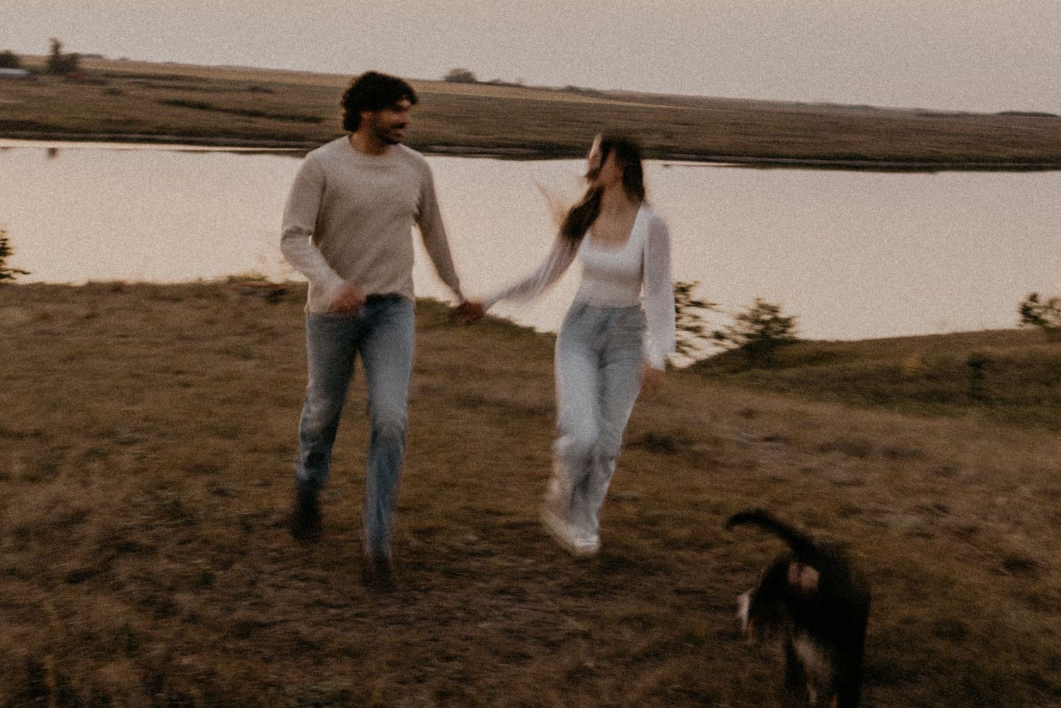 Casual couple walking on coastal trail with black dog at dusk.