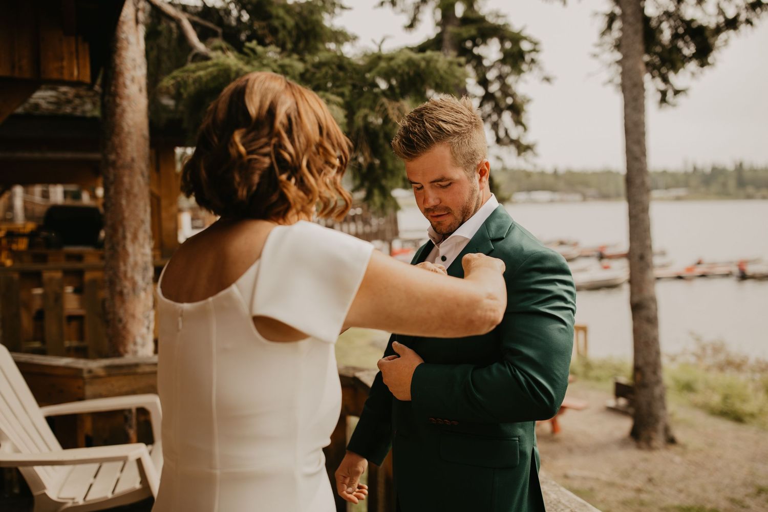 A couple shares an intimate first look moment outside near a lake with pine trees in the background.