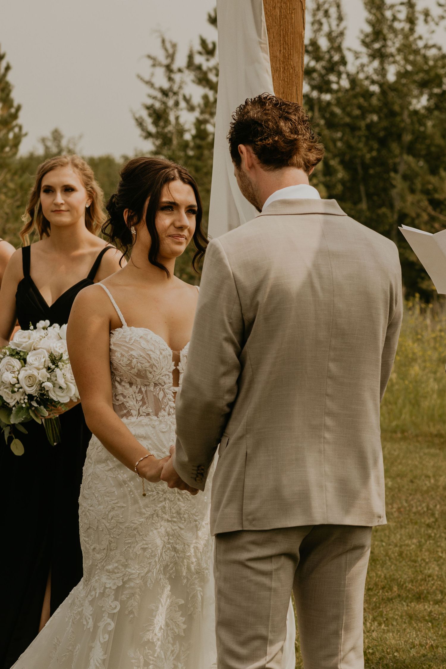Outdoor wedding ceremony under wooden arch with natural landscape backdrop.