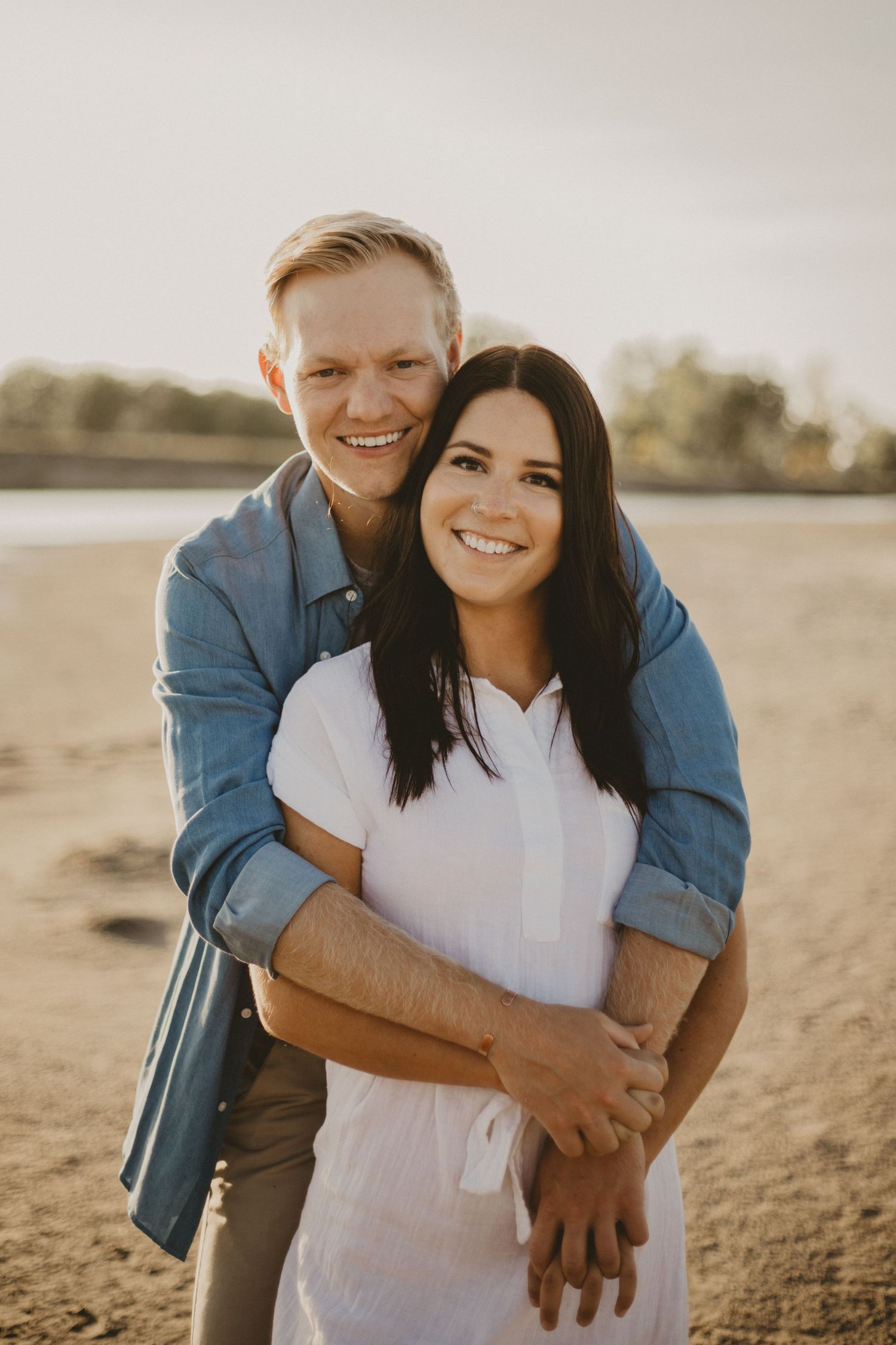 A romantic couple embraces on a beach at sunset with warm golden lighting.