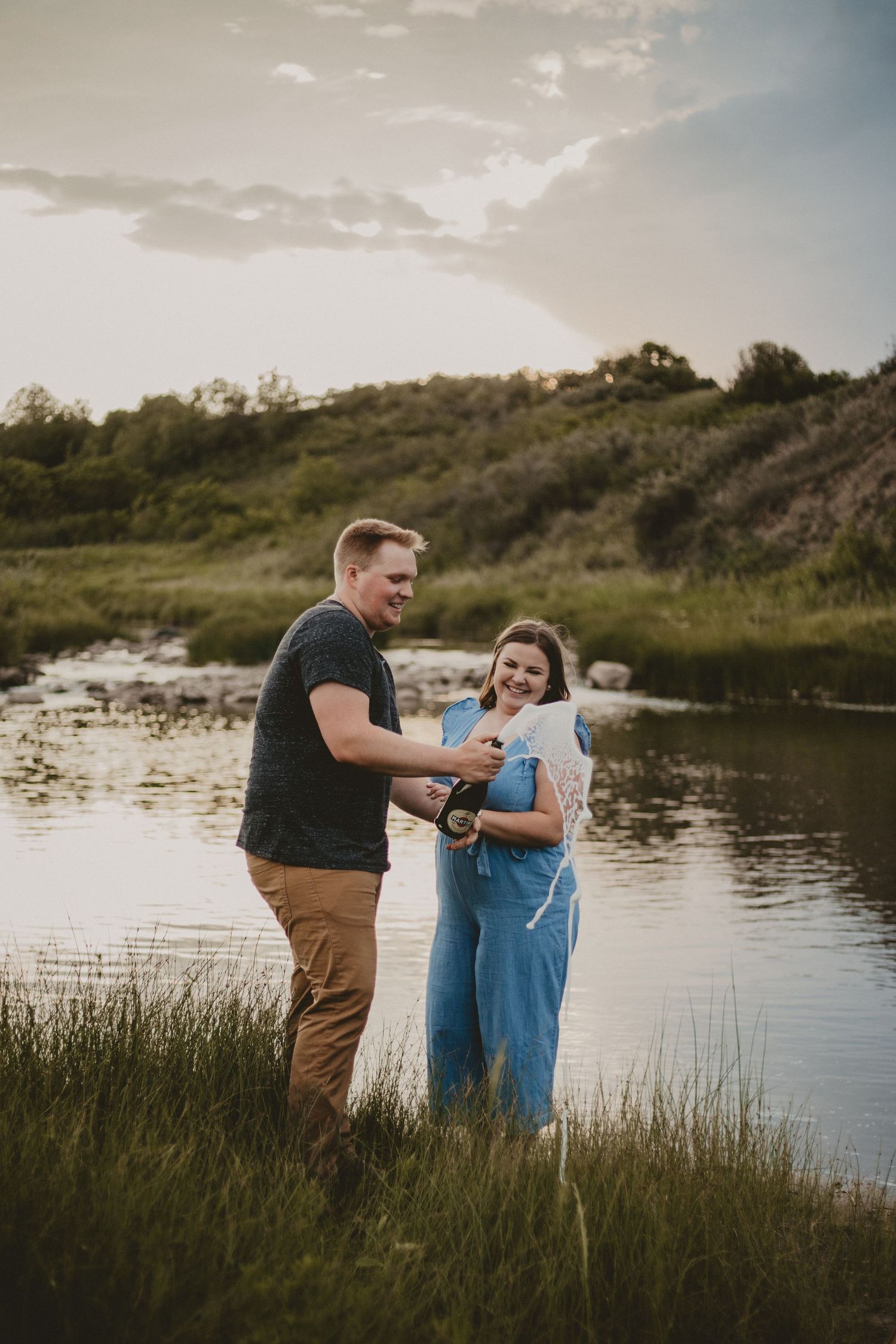 A playful moment captured between two people sharing drinks by a scenic lake at sunset.