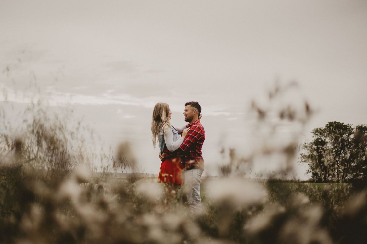 A dreamy countryside engagement photo with soft focus foreground elements.
