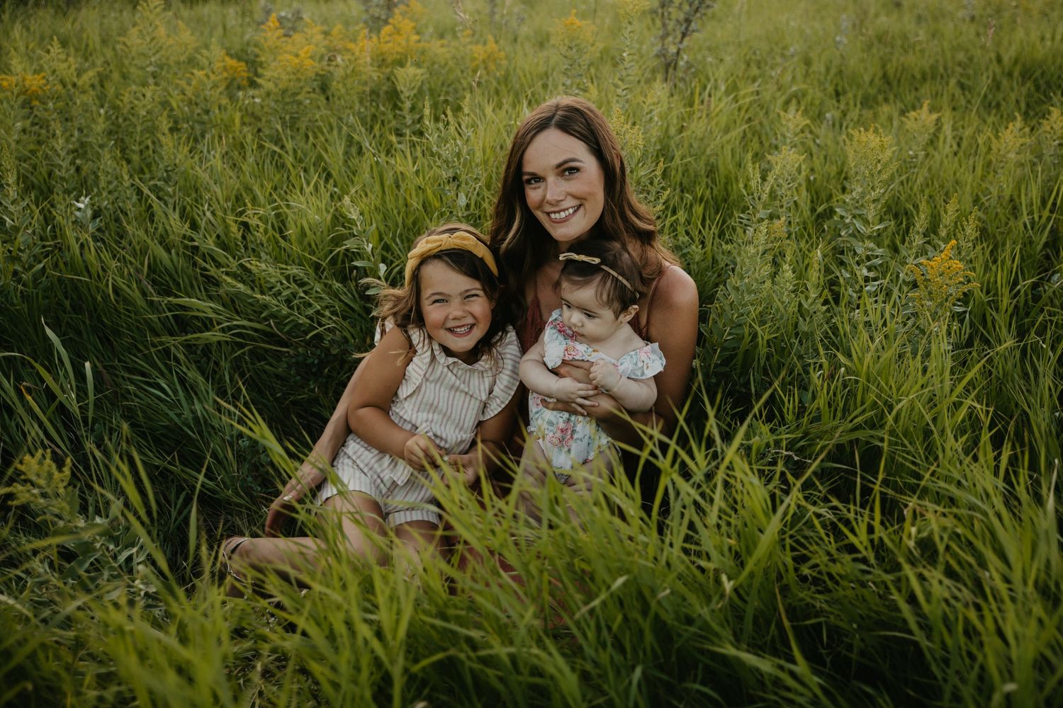 Family group seated in tall wild grass during golden hour.