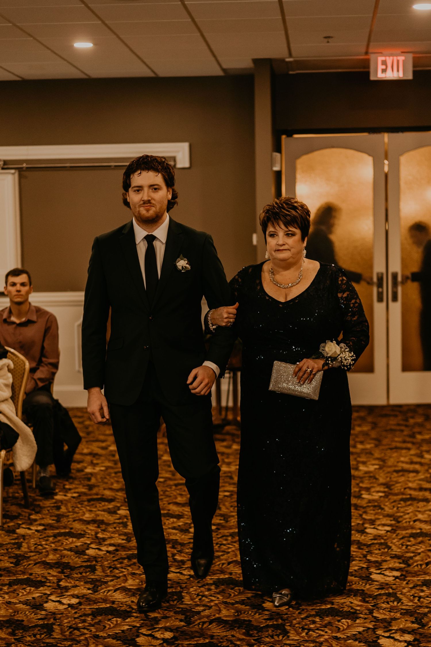 Wedding processional in a carpeted venue with ornate lighting and decor.