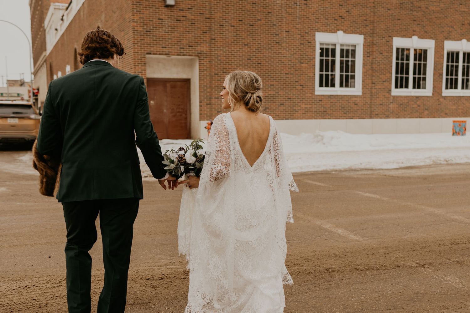 A couple in wedding attire walks away from a brick building on their special day.