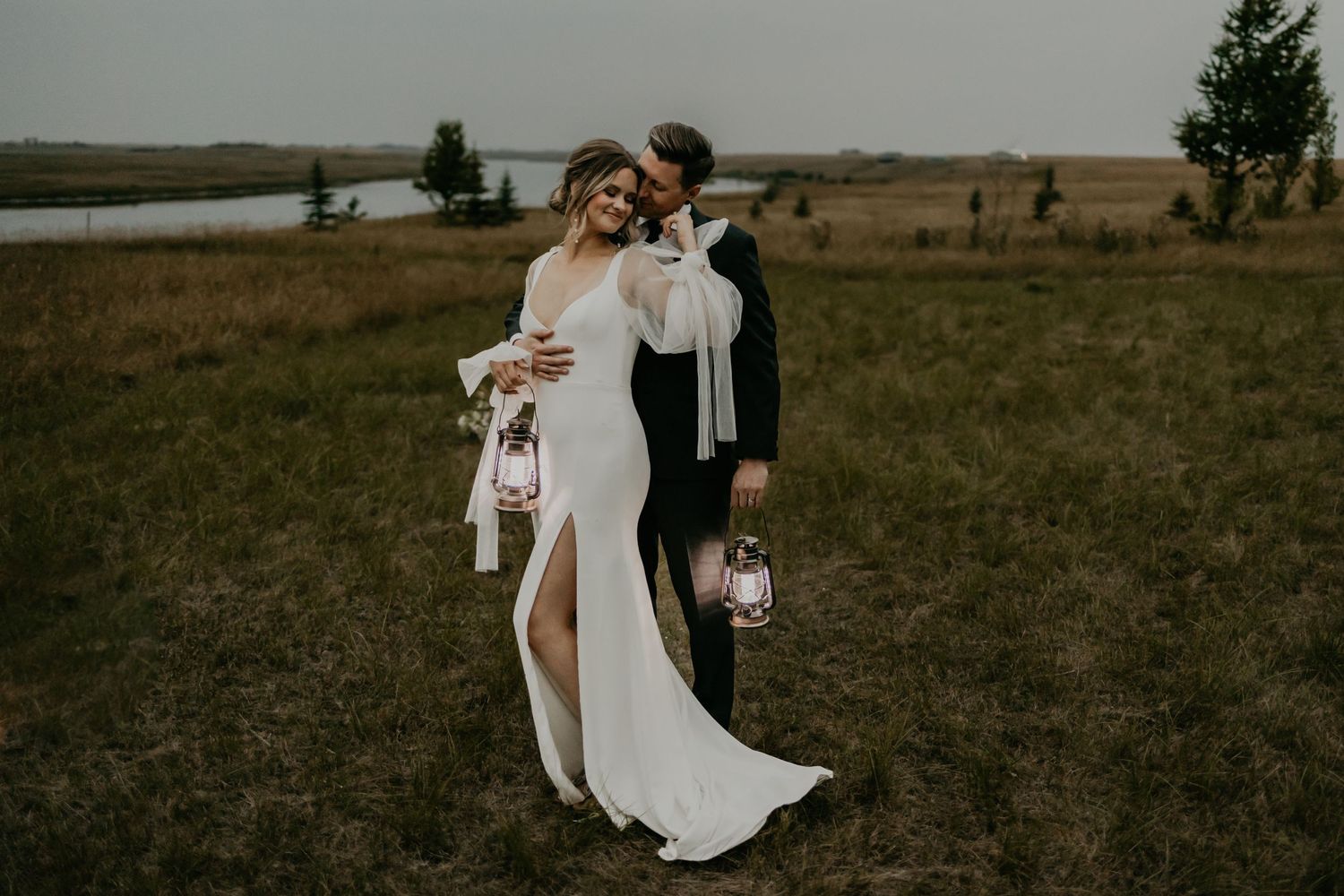 Romantic moment in flowing white wedding dress against rustic outdoor backdrop.