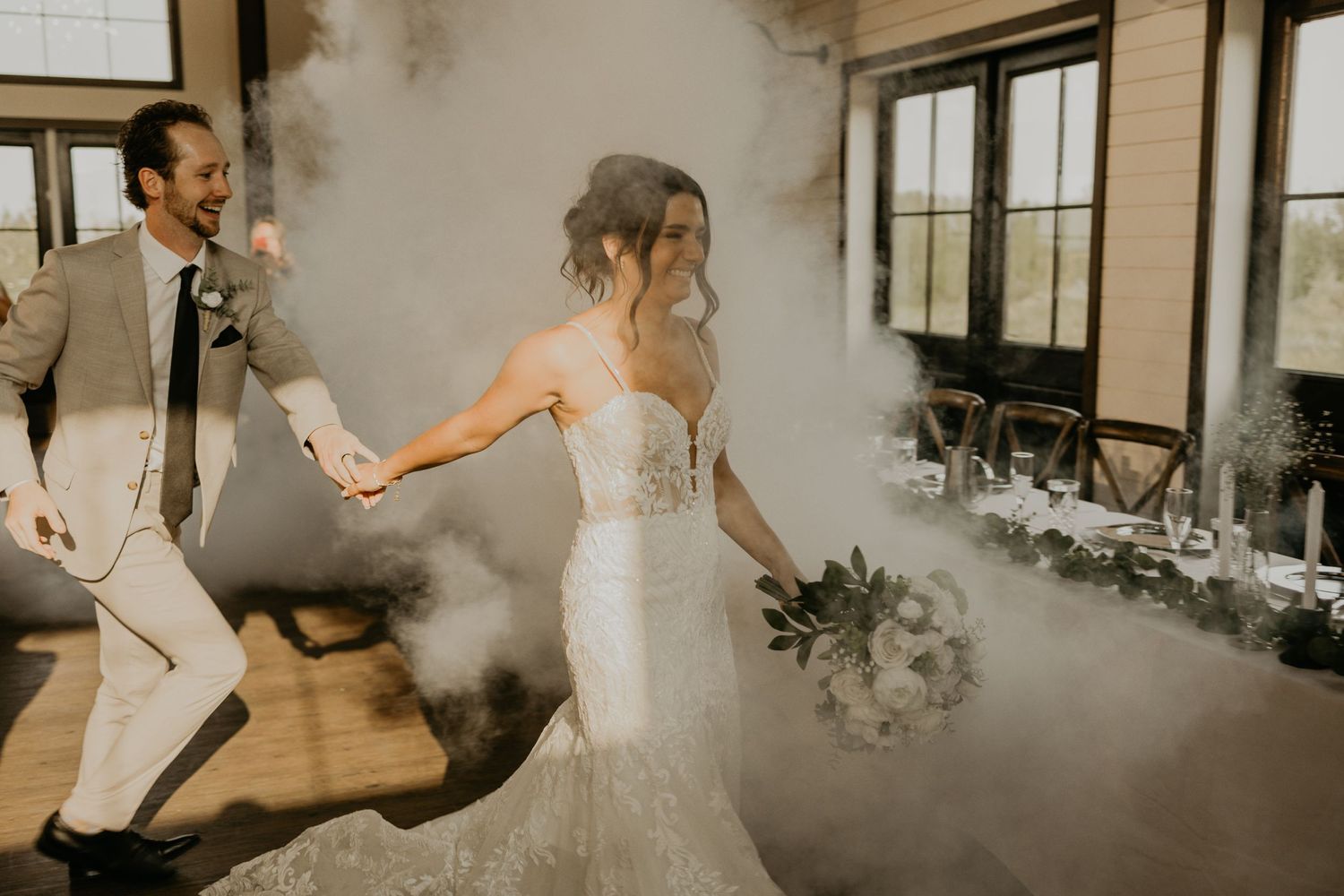 Bride in lace dress dances through dramatic smoke effects at wedding reception.
