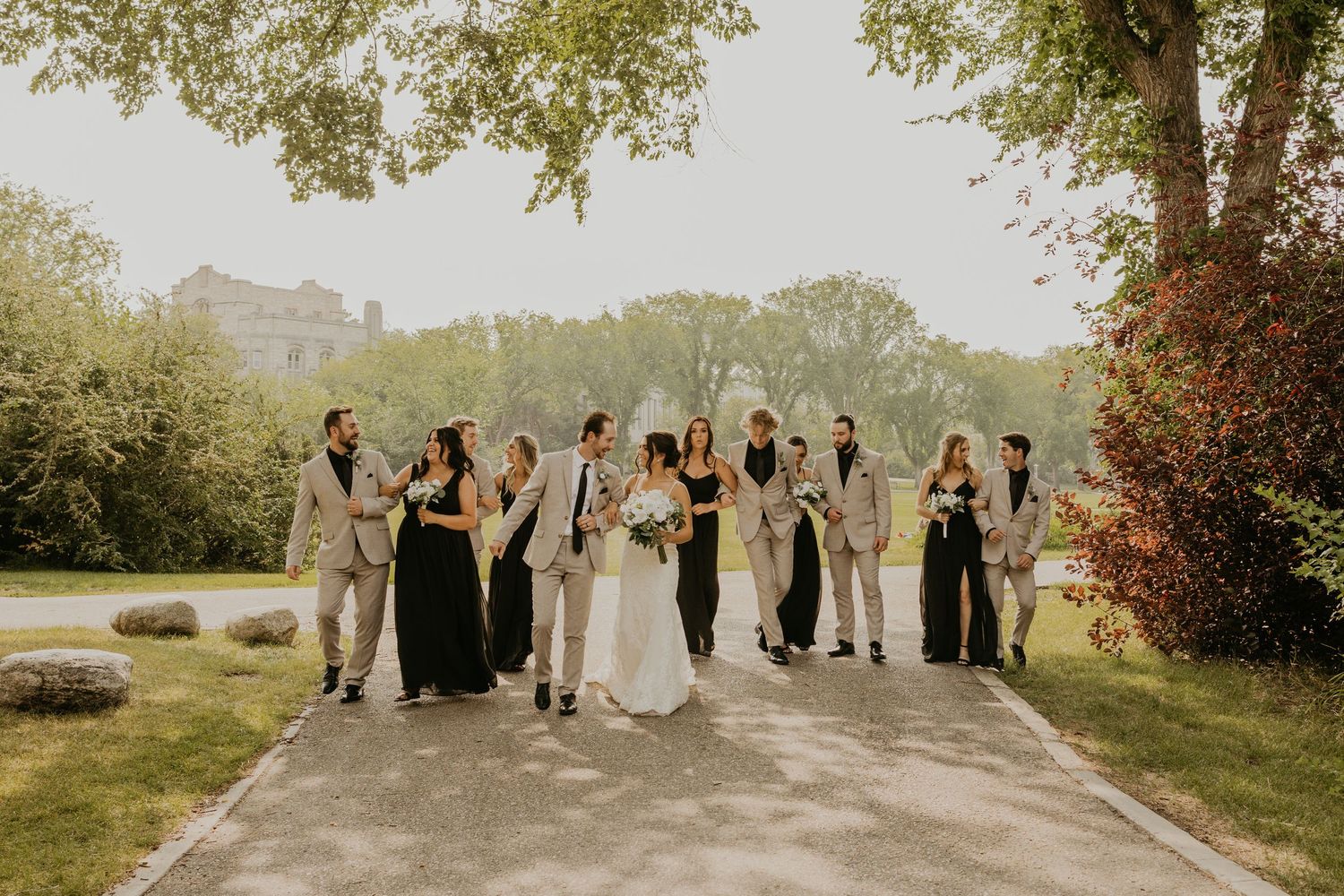 Wedding party celebrating with arms raised on stone path surrounded by greenery.