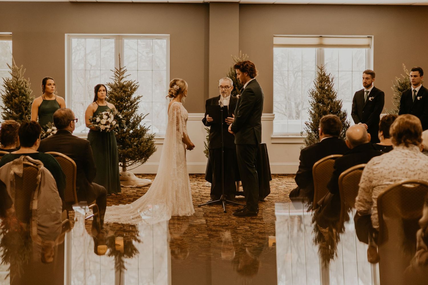 Wide shot of wedding ceremony with Christmas trees and seated guests.