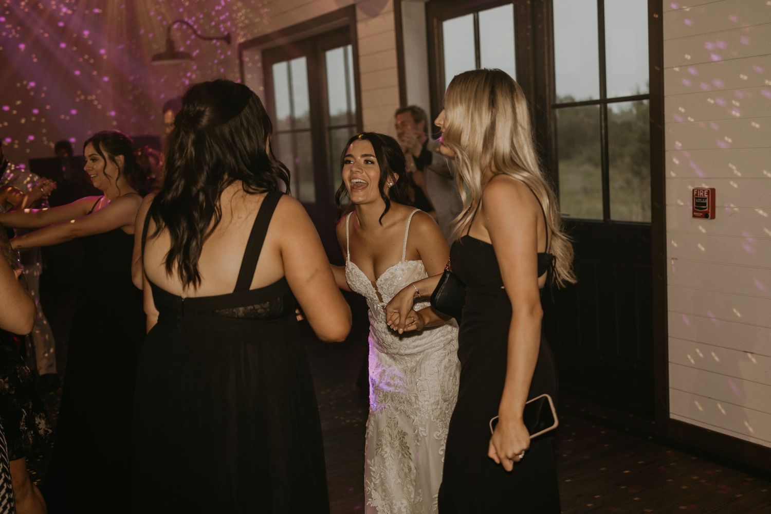 Wedding guests dancing together at a reception with purple mood lighting.