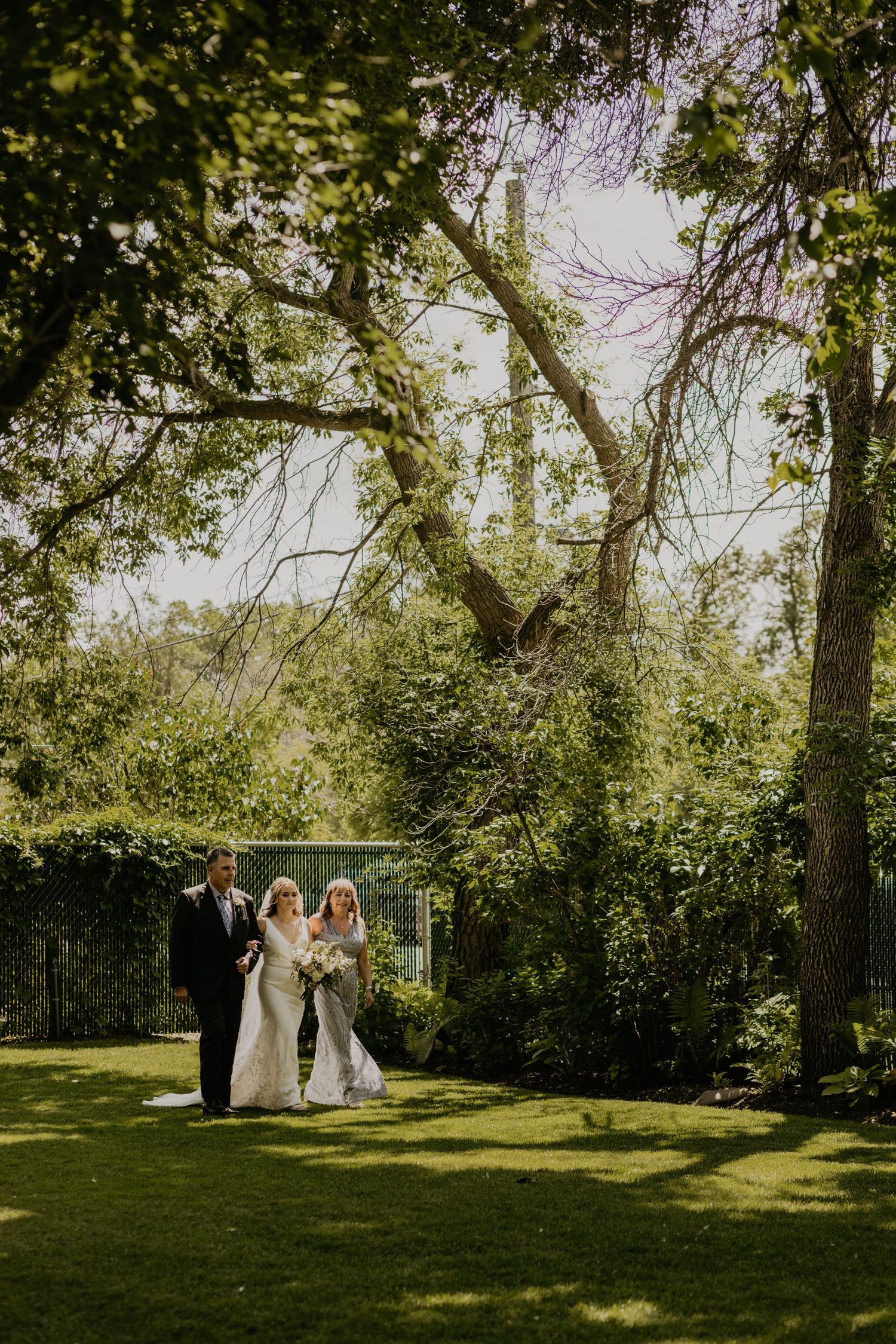 Outdoor garden wedding ceremony under tall trees with golden sunlight filtering through the leaves.