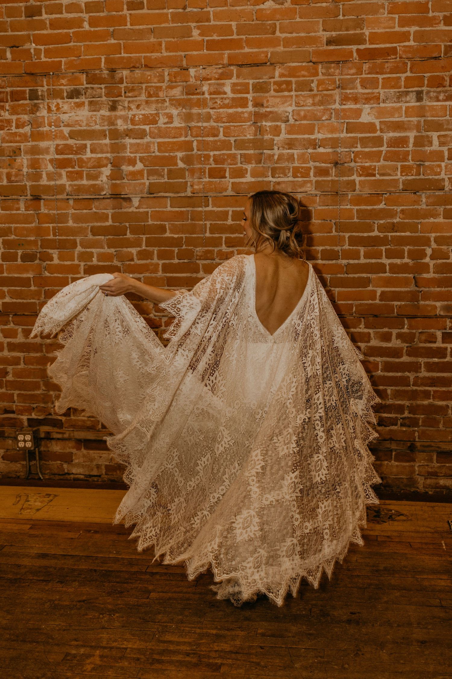 Back view of a lace wedding dress spinning against a rustic brick wall background.