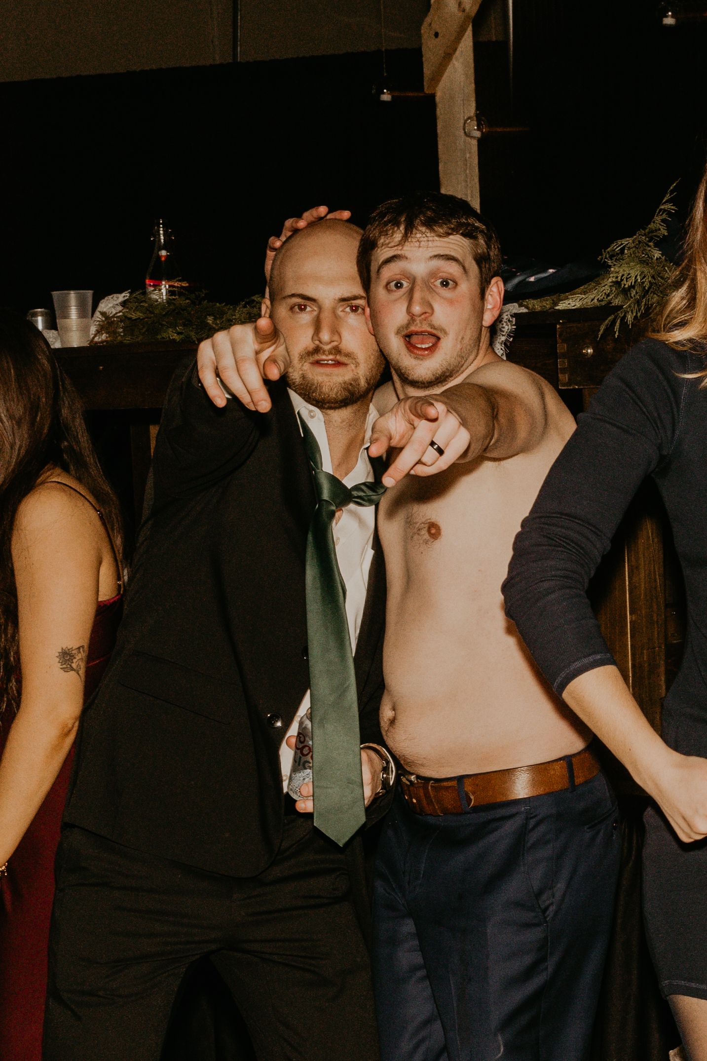 Two party guests posing together at a celebration wearing formal attire and making animated expressions.