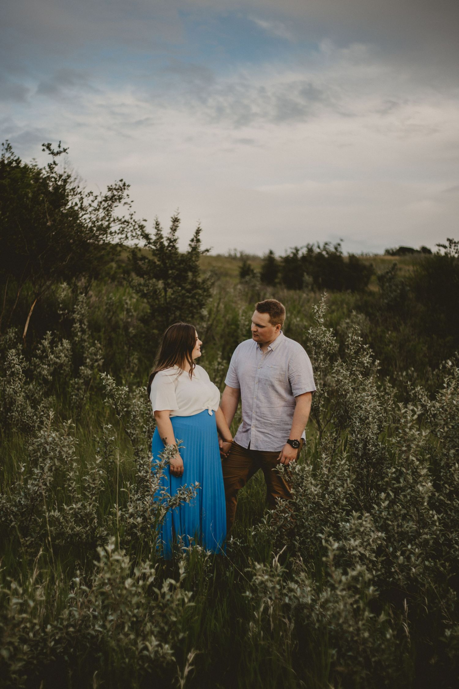 A couple shares a tender moment while standing in a wild meadow at dusk.