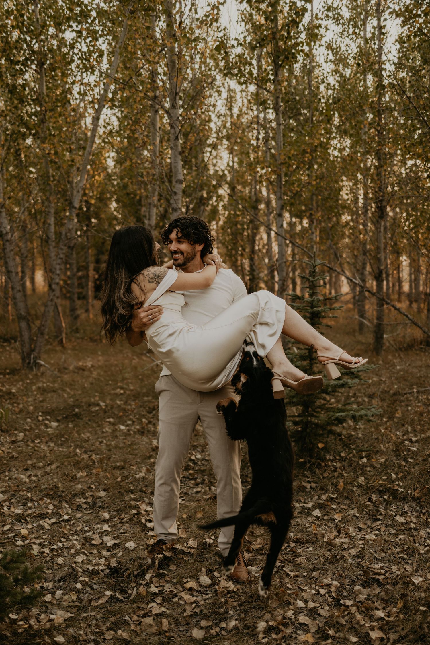 A romantic couple dancing playfully together in a scenic wooded area during golden hour.