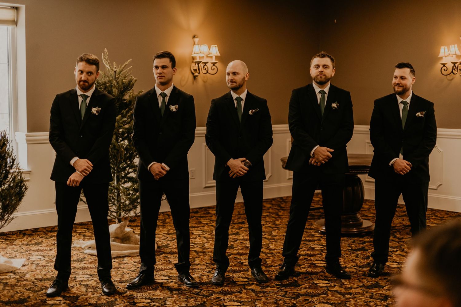 Groomsmen in black suits stand in a line during formal wedding ceremony.