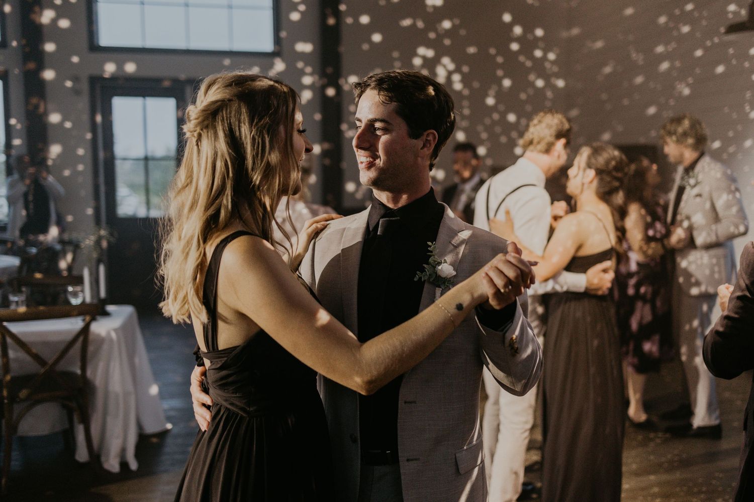 Wedding guests dance together under sparkling lights at an evening reception.