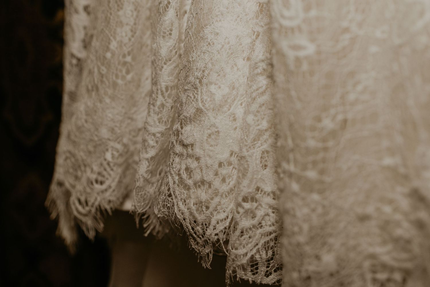 A woman in a white robe reaches up to touch a hanging wedding dress.