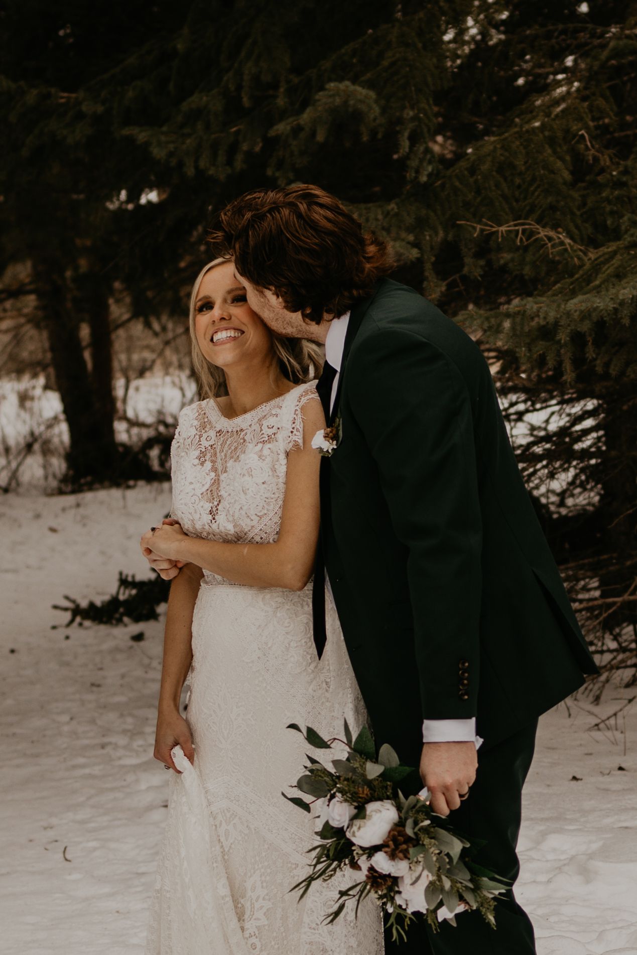 A romantic moment between newlyweds as they share laughter in a snowy forest setting.