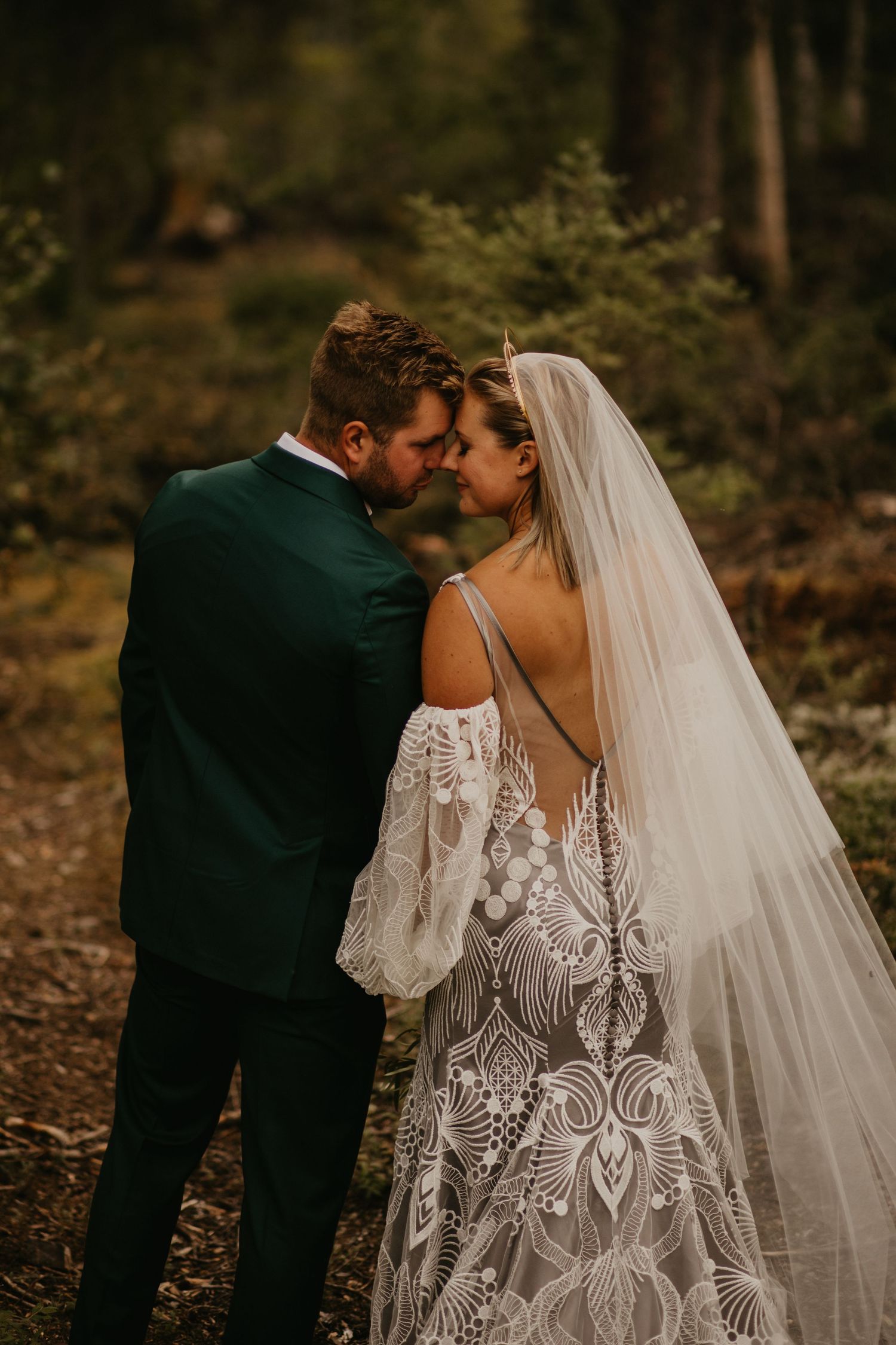 Intimate moment between newlyweds showcasing detailed lace wedding dress and emerald suit.
