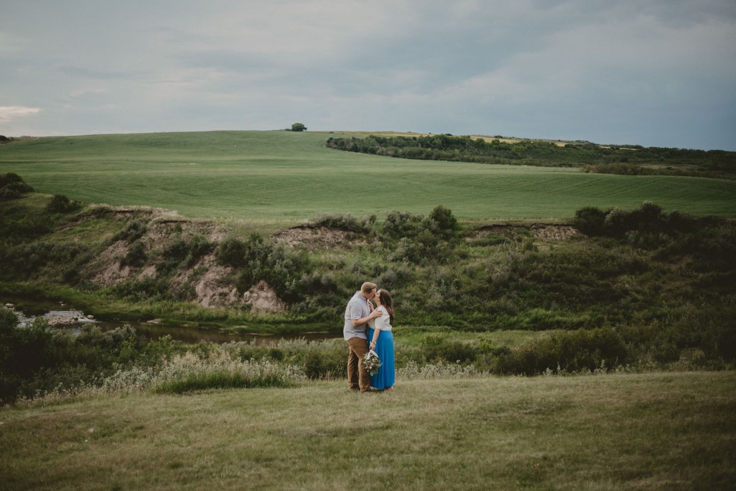 Couple shares tender moment on rolling green hills during golden hour.
