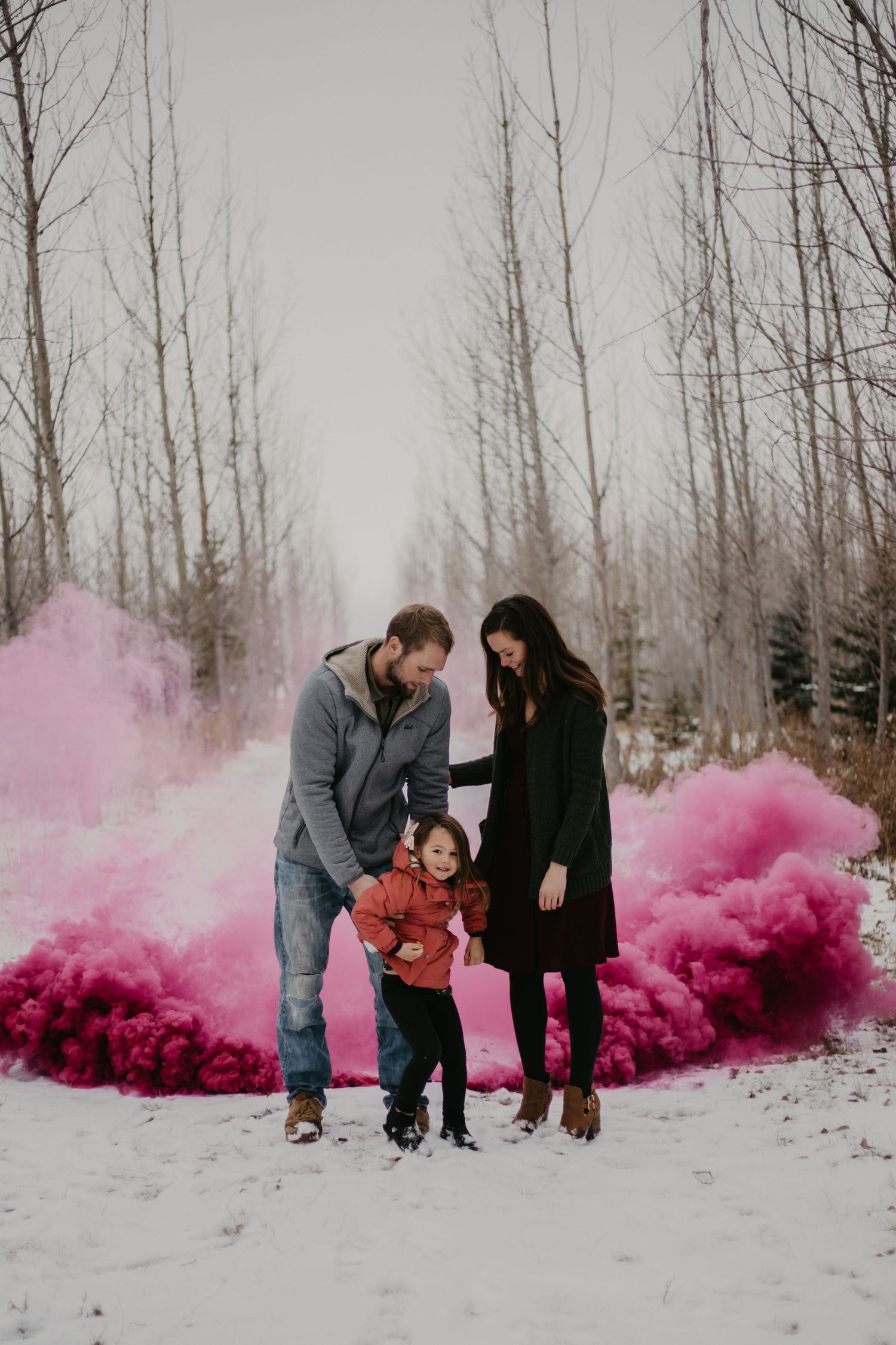 A family stands together surrounded by bright pink smoke in a snowy winter forest.