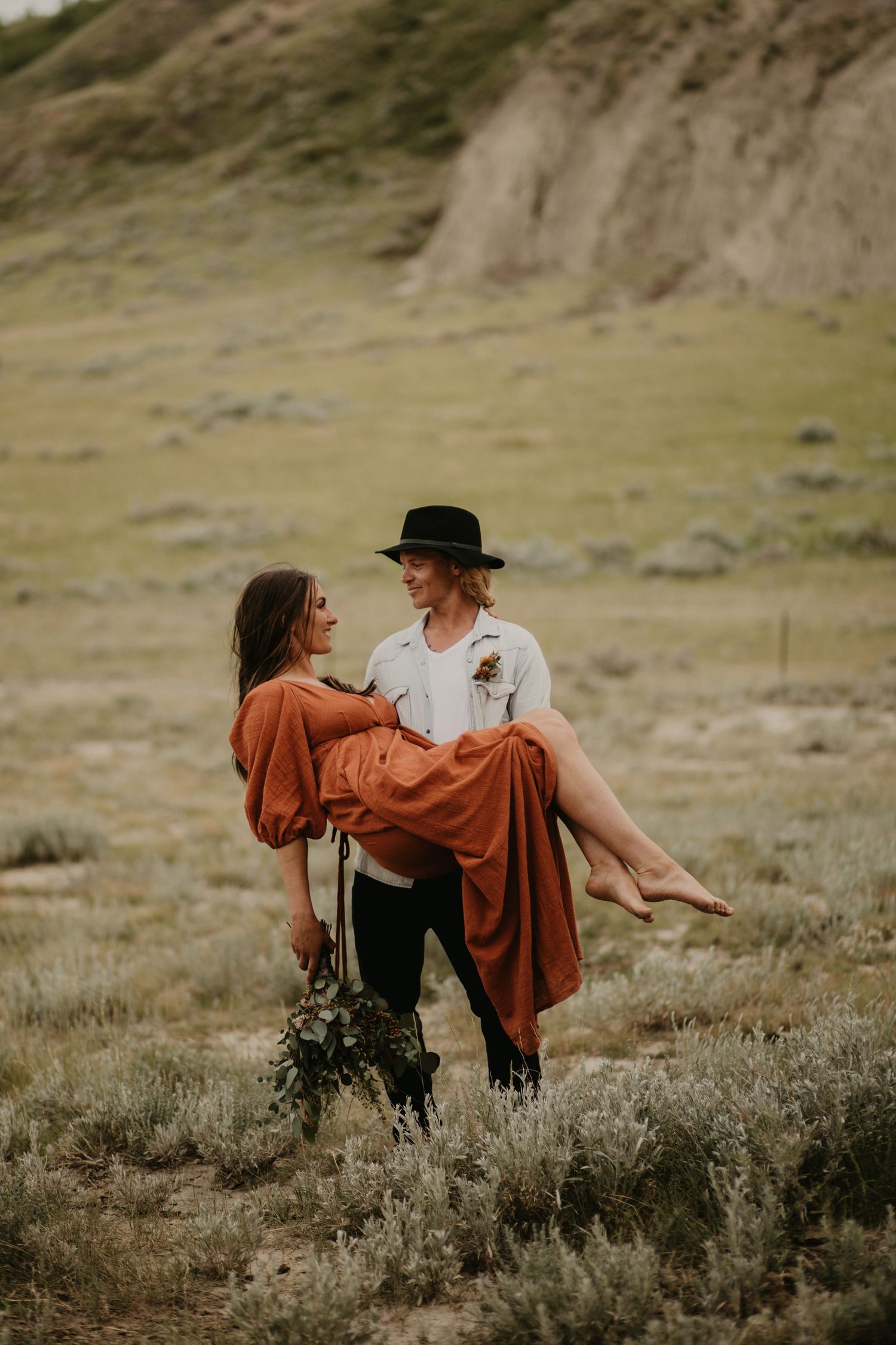 Person in flowing rust dress being carried in rustic outdoor setting.