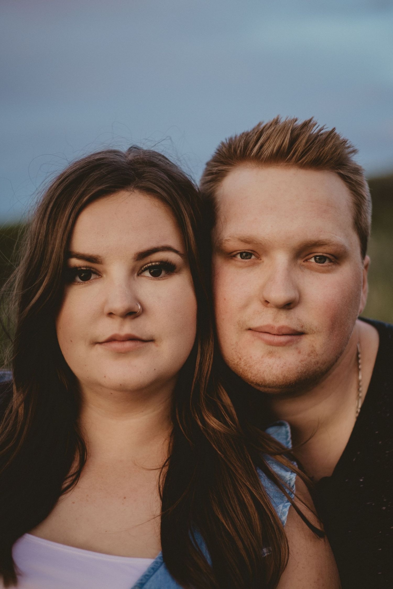 Close-up portrait of a couple against a dusky sky background.