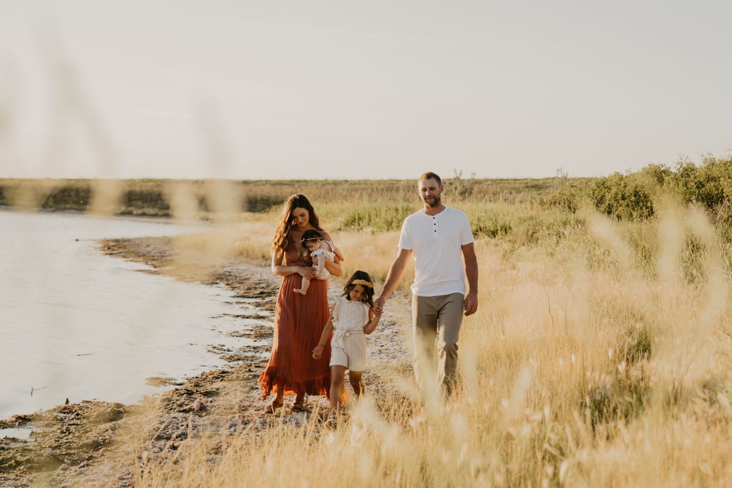 Family walking together along shoreline path during golden hour sunset.