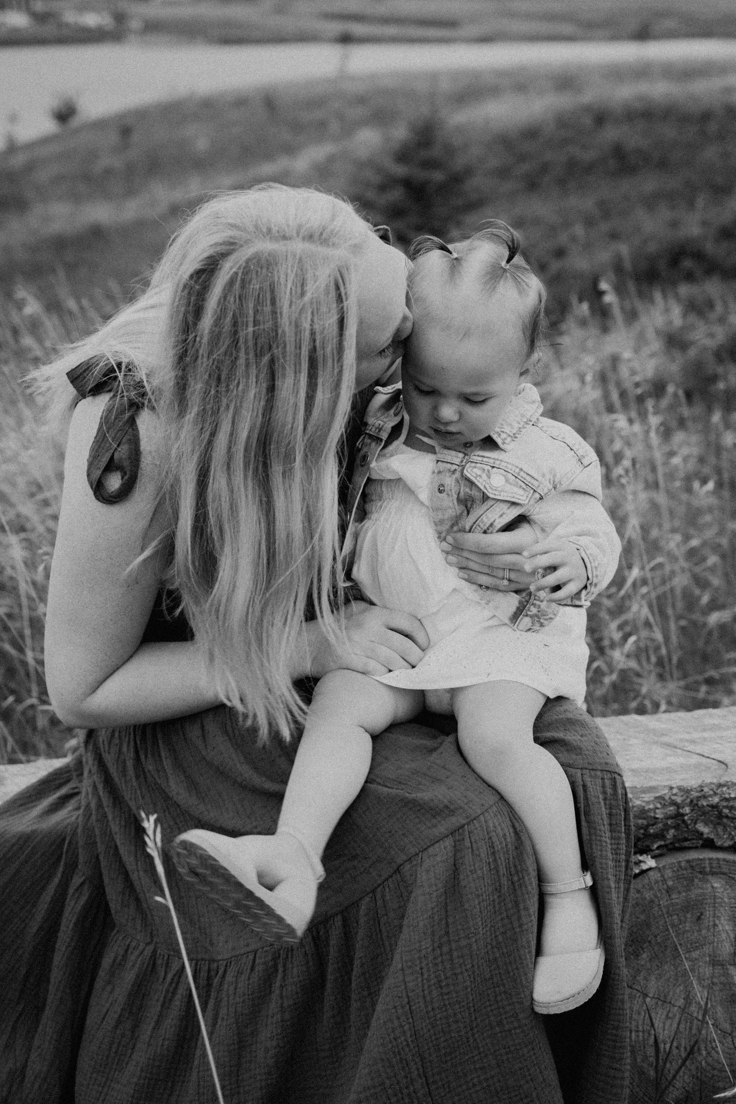 A tender moment between parent and child sitting outdoors in a field.