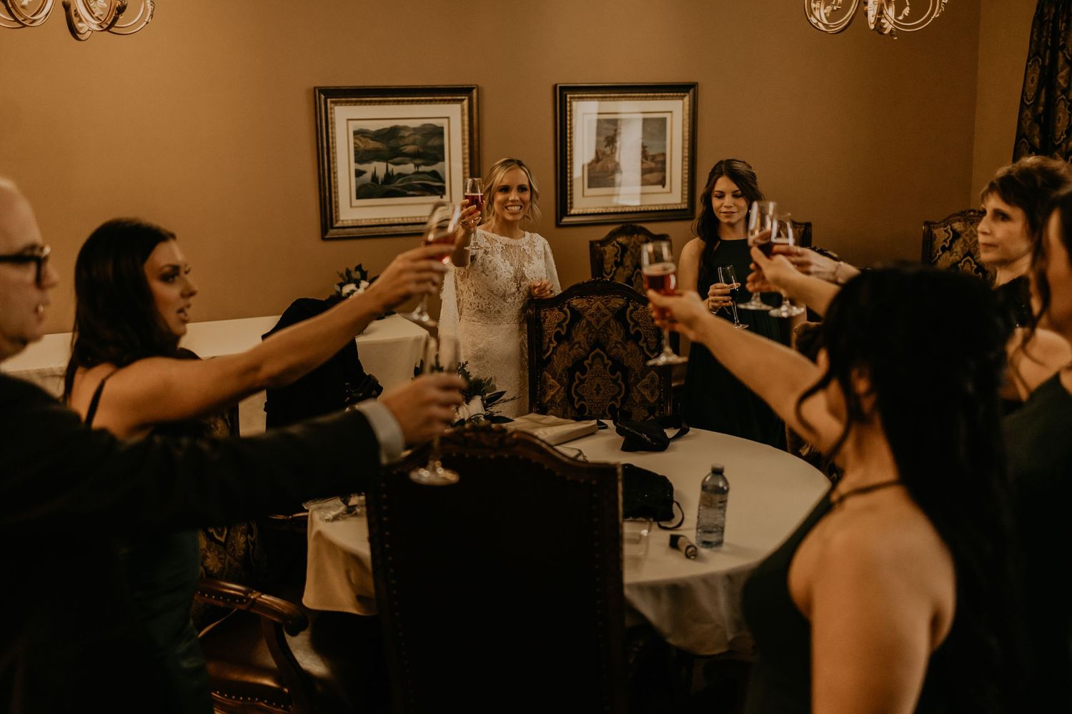 Wedding party raises glasses in a celebratory toast around a table.