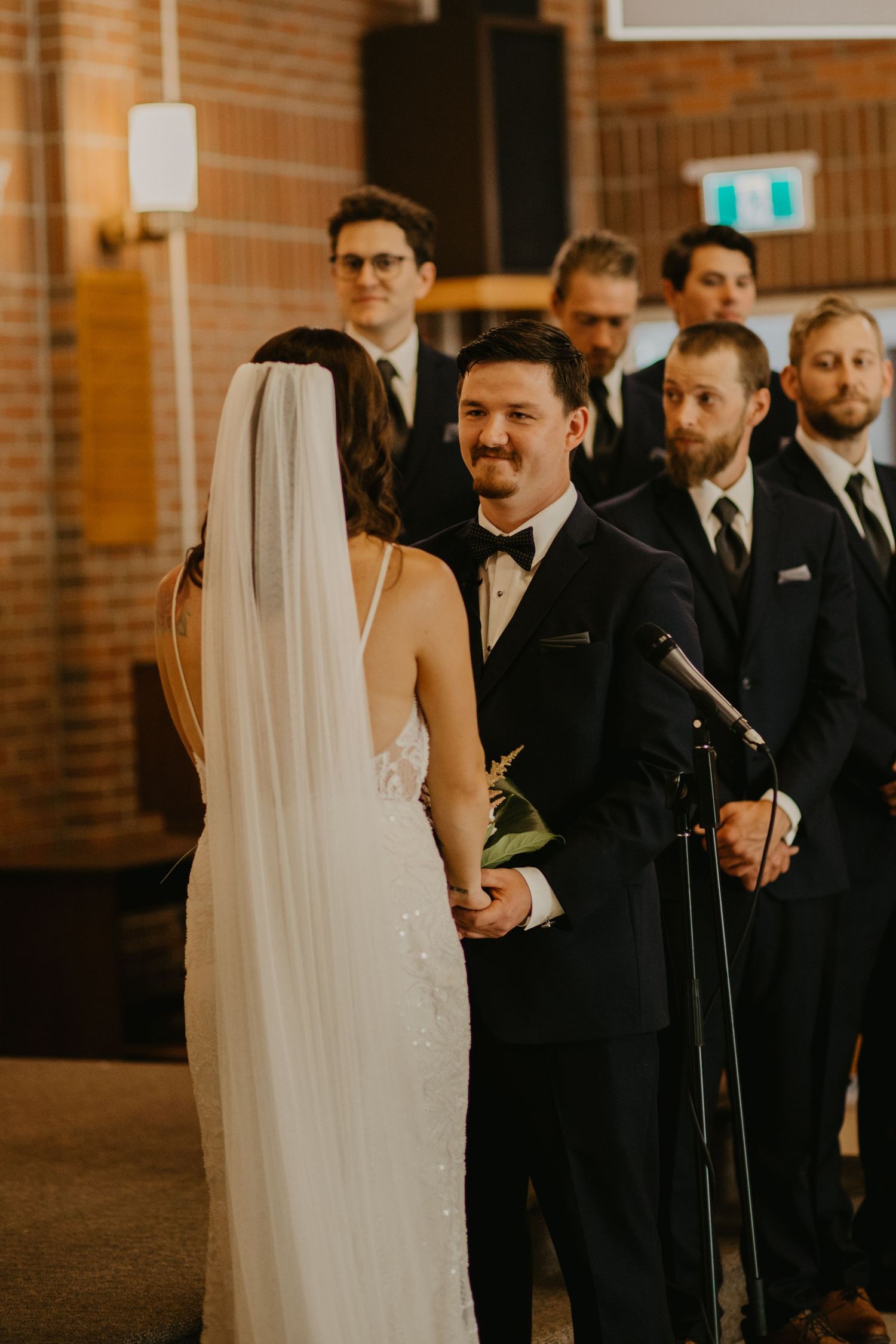 A wedding ceremony scene in a brick-walled venue with elegant formal attire.