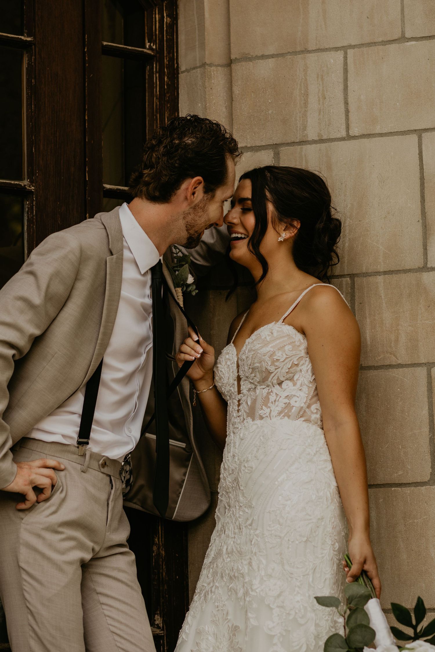 Intimate moment between couple against stone wall in wedding attire.