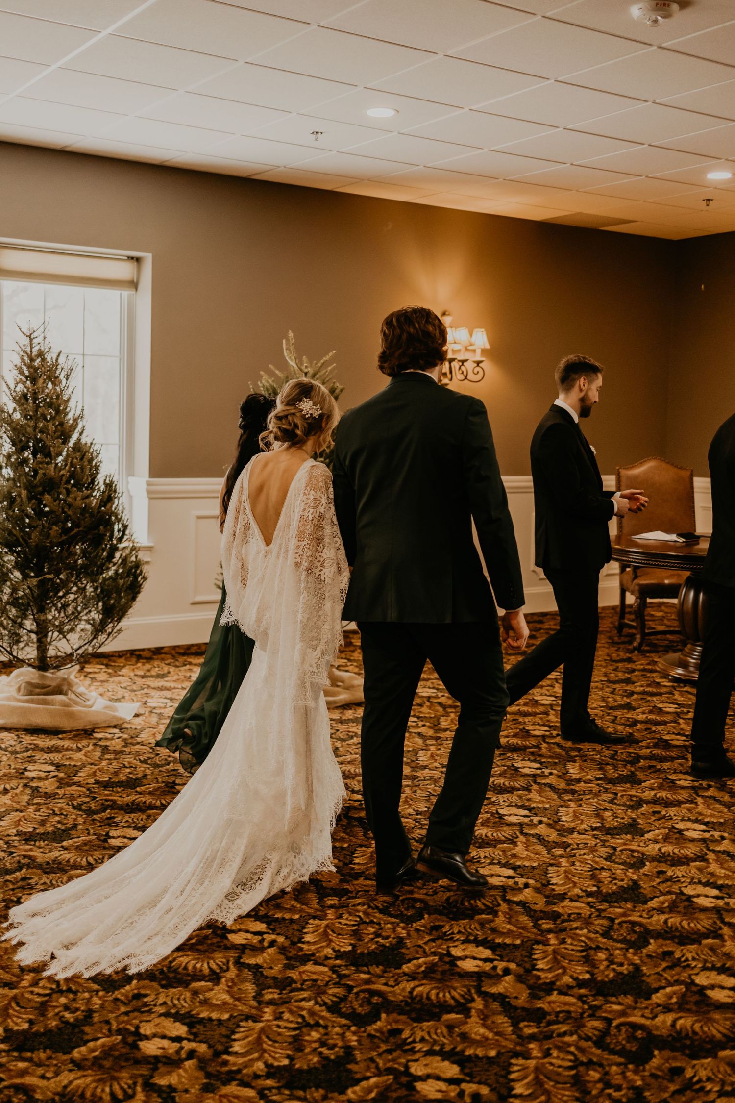 Couple walks through venue with trailing lace wedding dress and Christmas decor.