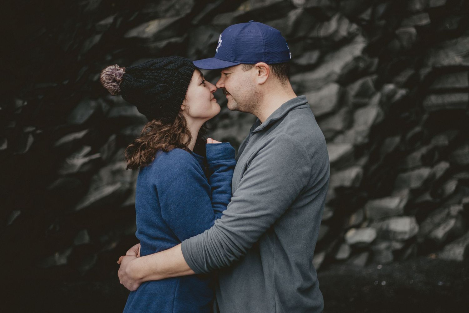 An intimate moment between a couple as they embrace and lean in close against a moody dark background.