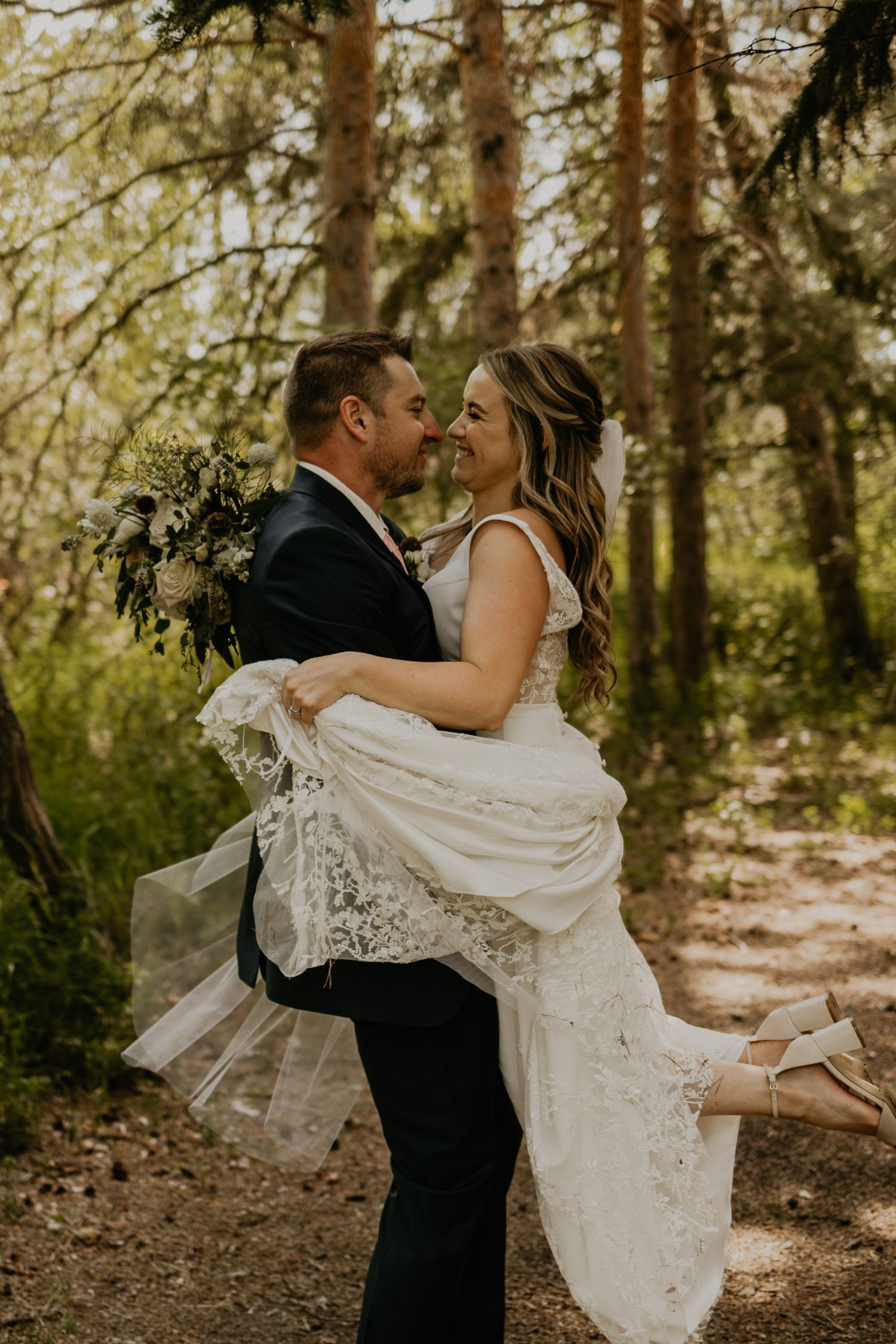 A joyful moment between newlyweds on a forest path with white floral bouquet.