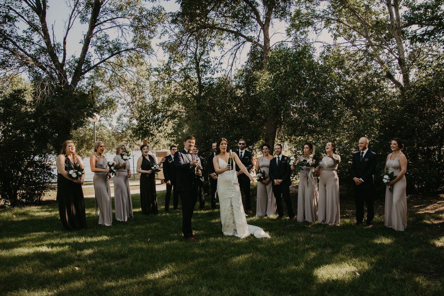 Wedding group poses in natural setting with soft lighting filtering through trees.