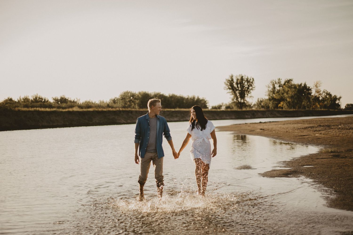 Couple walking together in shallow water during sunset at a peaceful beach.