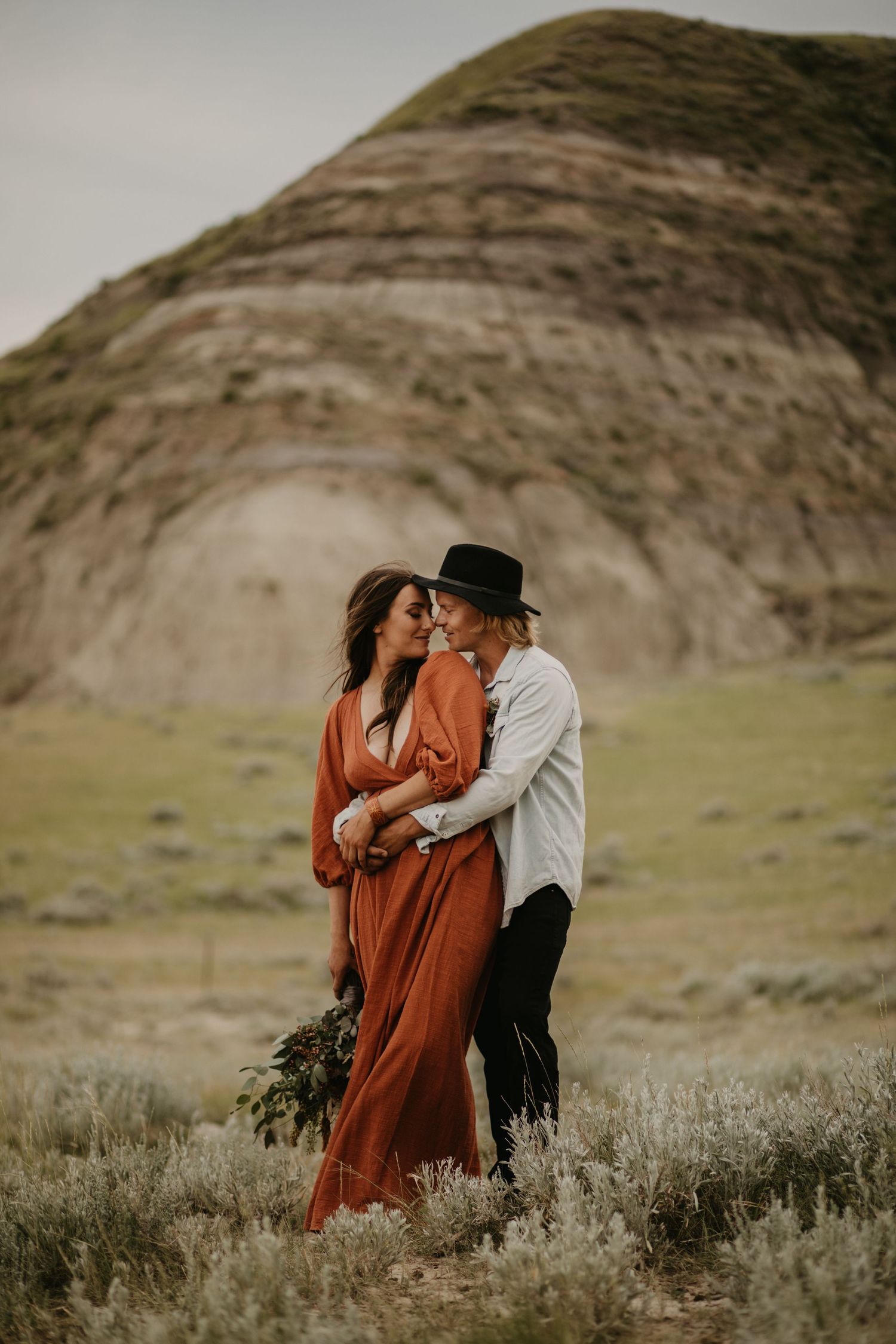 A couple embraces in front of a towering desert cliff with dramatic lighting.
