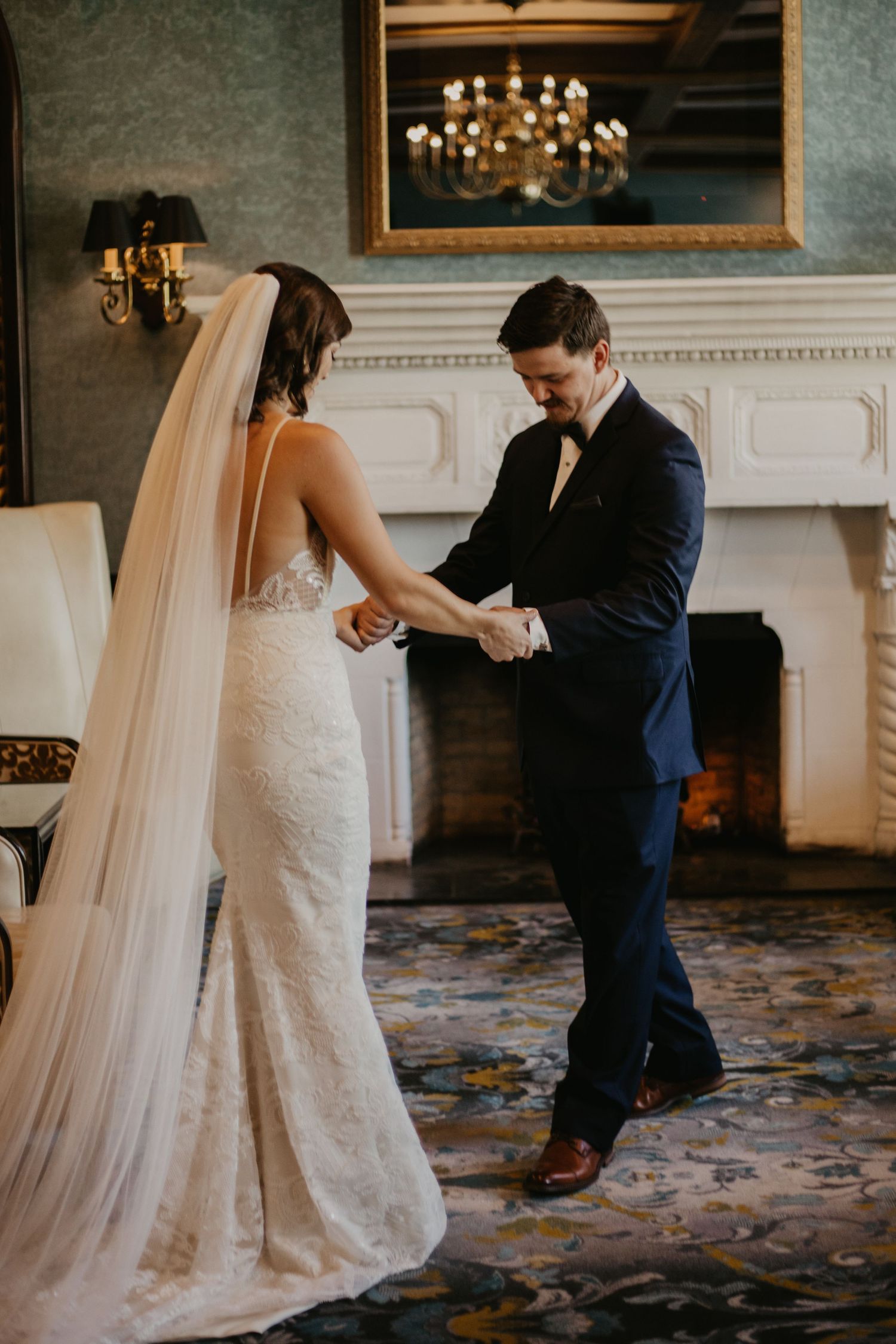 A tender first look moment between newlyweds in an elegant room with a white fireplace.