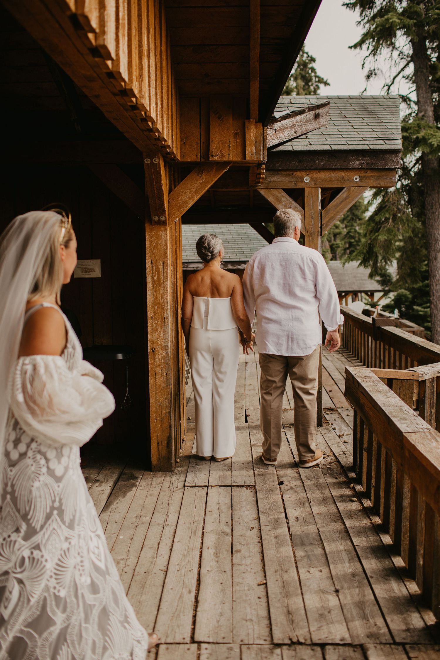 Wedding party members in white attire standing on wooden deck overlooking scenic view.