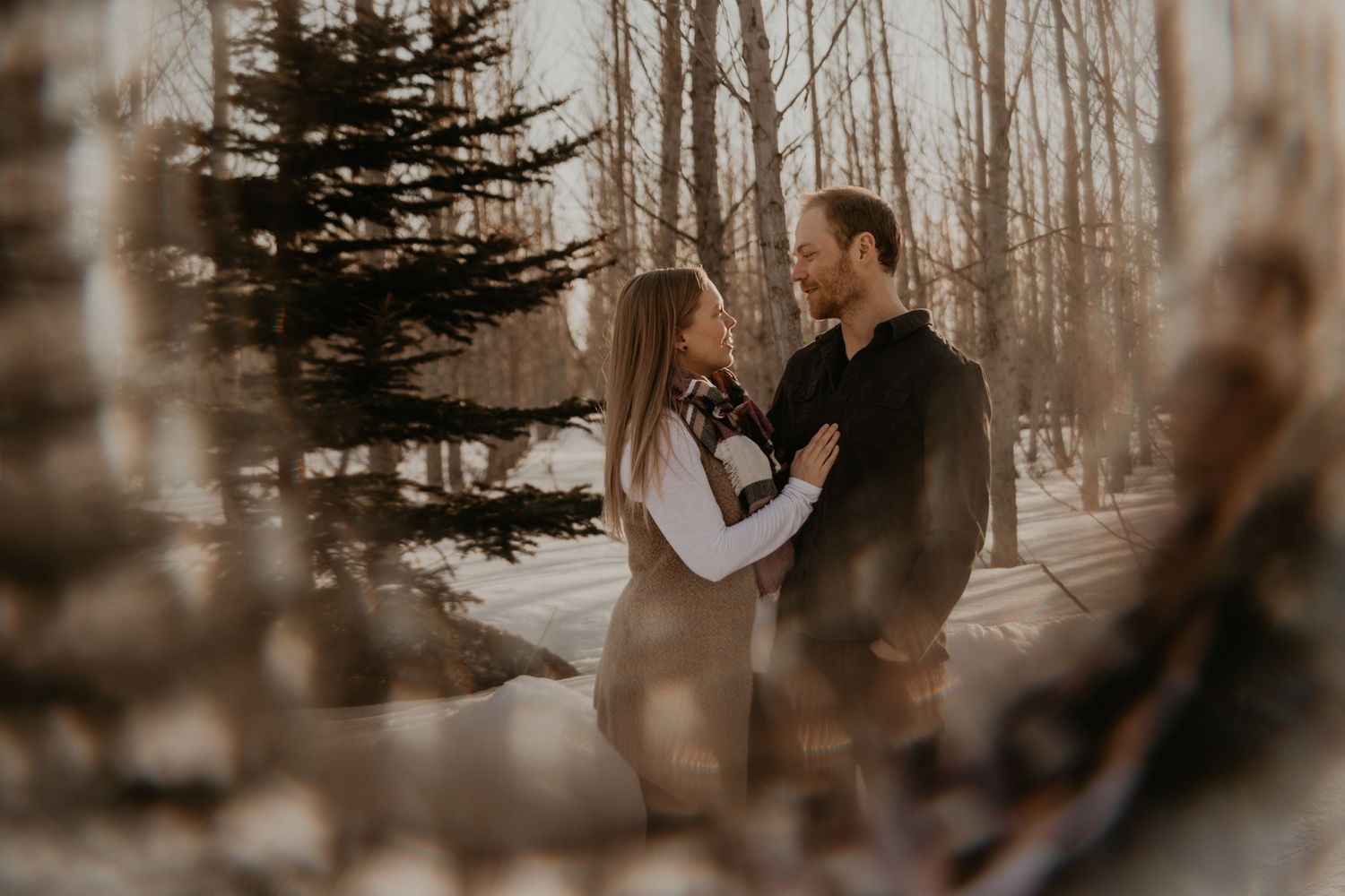 A couple shares an intimate moment in a snowy forest setting.